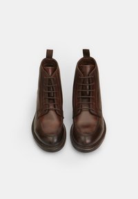 Botine din piele maro, cu vârful rotund, șireturi în față, detalii cusute și fanta de prindere la spate. Textură netedă și talpă rezistentă.