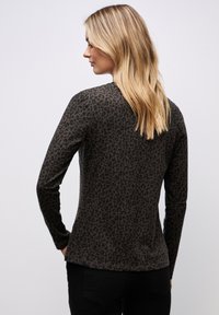 Långärmad, figurnära topp i mörkgrön med svart leopardmönster. Mjuk tyg med rund halsringning och böjd fåll.