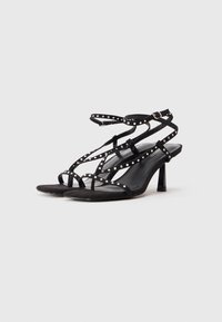 Sandale cu toc din suede negru, cu mai multe curele încrucișate ornate cu bosete argintii strălucitoare, având un toc înalt subțire și un design cu vârf deschis.