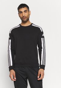 Svart hettegenser med lange ermer, har hvite tre-stripes detaljer langs skuldrene og armene, laget av et mykt stoff.