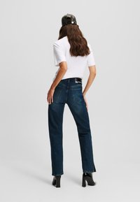 Dark blue denim jeans with a straight cut, featuring a high waist, two back pockets, and subtle contrasting stitching. Pair worn with a white t-shirt.
