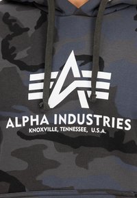 Kapucnis pulóver sötétszürke és fekete kamuflázs mintával. Fehér logó és felirat található a mellrészen, a húzózsinórok pedig egy megfelelő sötét színben készültek.