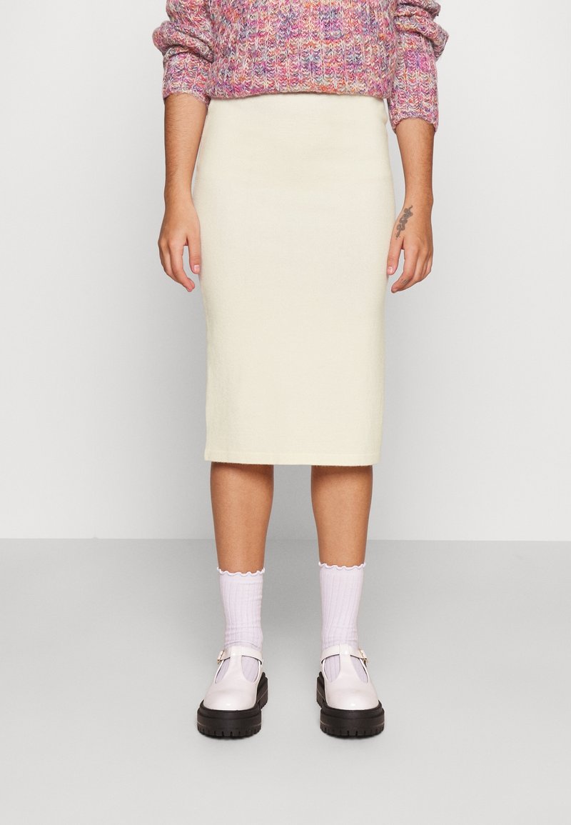 Knee-length cream pencil skirt with a smooth texture. Paired with white ribbed socks and shiny lilac shoes featuring a buckle detail.