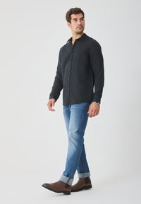 Dunkelblaues Hemd mit Knopfleiste, kombiniert mit hellblauen Jeans und braunen Stiefeletten. Jeans an den Säumen hochgekrempelt. Einfacher und klarer Look.