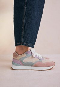 Multicolored sneaker featuring pink, blue, and beige suede panels, white laces, and a prominent white sole with a textured brown bottom.