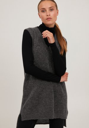 Gray sleeveless sweater vest with a soft texture, featuring a rounded neckline and side slits. Worn over a black long-sleeve top.