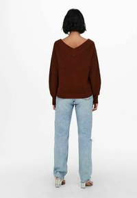 Pull en tricot marron avec col en V, associé à un jean large bleu clair. Le jean présente un ourlet effiloché et une légère usure.