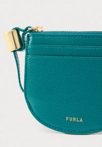 Rohelise nahaga mündikott tekstuurse pinnaga, kuldse tõmblukuga ja metallist riistvaraga. Omab väikest rihma ja põhjas reljeefset brändinime.