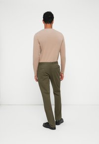 Jasnobrązowa koszula z długim rękawem w połączeniu z oliwkowymi spodniami. Spodnie mają dwie tylne kieszenie i są szyte w prostym kroju. Czarne buty.