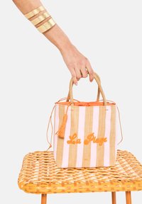 Vävt stråväska med rosa och beige ränder, orange snöre och frans. "La Plage" broderat i orange på framsidan.