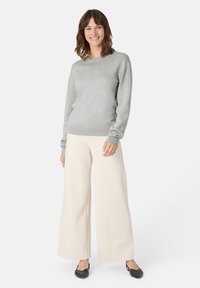 Světle šedý svetr s kulatým výstřihem a žebrovanými manžetami, doplněný širokými krémovými kalhotami. Černé baleríny dotvářejí vzhled.