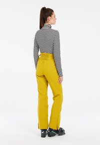 Juoda ir balta dryžuota golfo tipo palaidinė, derinama su aukšto liemens, garstyčių geltonumo kelnėmis, turinčiomis šonines skyles, ir juodais slidinėjimo batais.