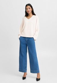 Lichtroze en witte gestreepte oversized trui met een V-hals, gecombineerd met wijduitlopende blauwe denim jeans en zwarte puntige hakken.