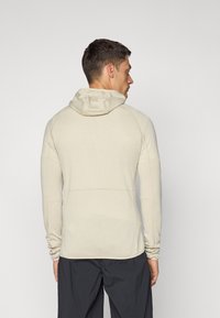 Pull à capuche beige clair, en tissu texturé avec des rayures horizontales, manches raglan et silhouette ajustée. Semble léger et sportif.