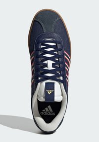 Navy blue sneaker with a textured upper, white and red stripes, and a rubber sole. Features a padded collar and tongue with branding.
