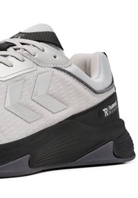 Sneaker sportivo grigio e nero che mostra dettagli laterali, suola spessa, colletto imbottito, lacci e loghi del marchio sulle parti superiori e sul tallone.