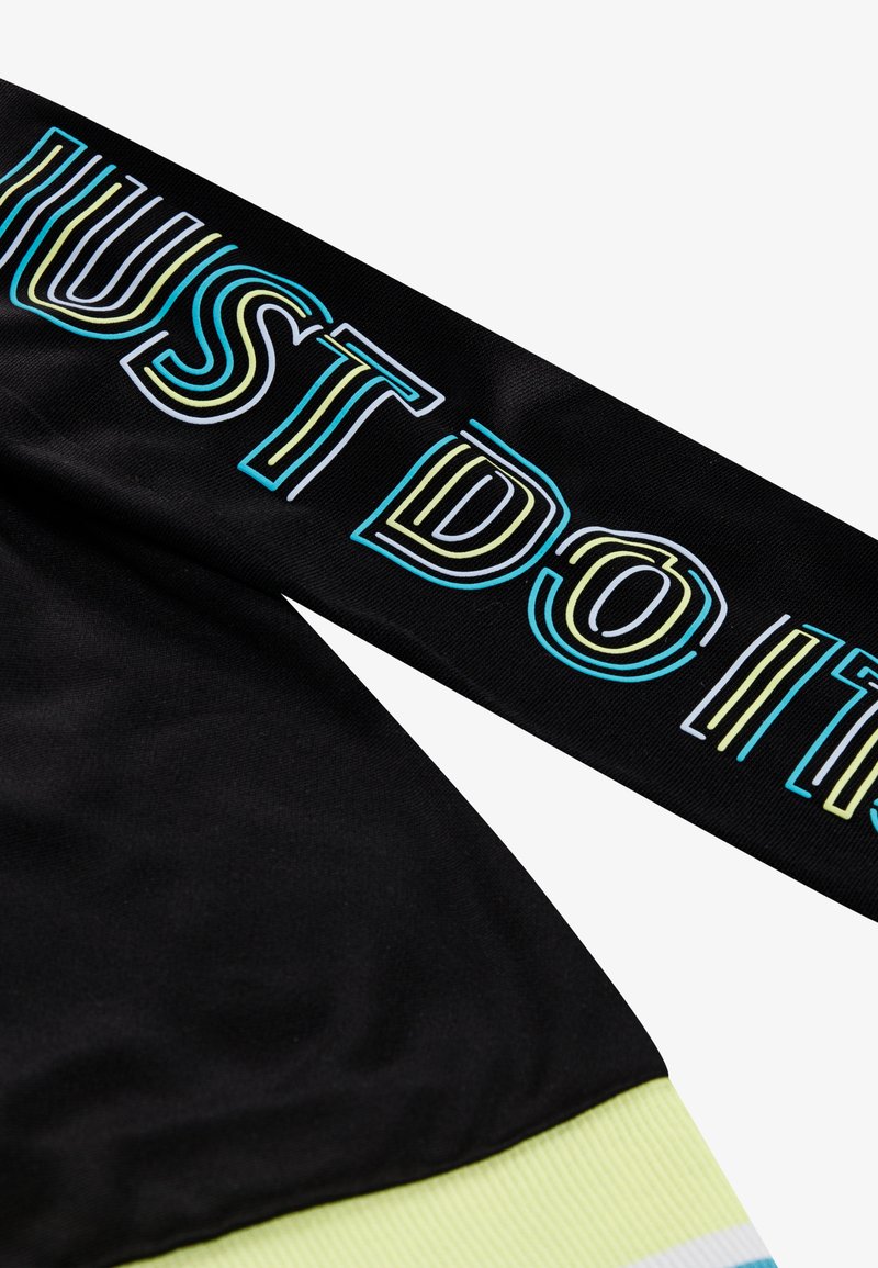 Prenda deportiva negra con el texto "JUST DO IT" en colores superpuestos. Detalles acentuados en un ribete verde claro en la parte inferior. Textura suave.