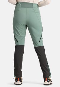 Grüne und schwarze Outdoor-Hosen mit Reißverschlüssen an beiden Seiten, aus flexiblem Material, mit hohem Bund und schmal zulaufendem Schnitt.