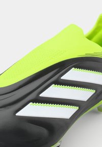 Black and neon green soccer cleat with a textured upper, featuring three white stripes and zigzag accents on the side. TPU outsole visible.