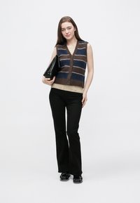 Bezrukávová pruhovaná vesta v tmavohnedej, modrej a krémovej farbe s výstrihom do V a zapínaním na gombíky. Kombinovaná s čiernymi nohavicami a čiernou kabelkou.