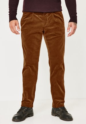 Man wearing brown corduroy pants, black leather boots, and a dark maroon long-sleeve top standing on a white background.