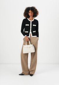 Svart cardigan med hvit trim og gullknapper, kombinert med beige vide bukser og en beige håndveske. Svarte leiligheter fullfører antrekket.