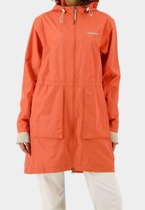 Imperméable à capuche orange avec fermeture éclair à l'avant et grandes poches, porté sur un pantalon blanc et manches de pull côtelé beige visibles aux poignets.