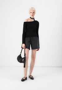 Zwarte off-the-shoulder top met lange mouwen, donkergrijze denimshorts, zwarte tas met hardware-accenten en zwarte platte schoenen met gaatjesdetails.