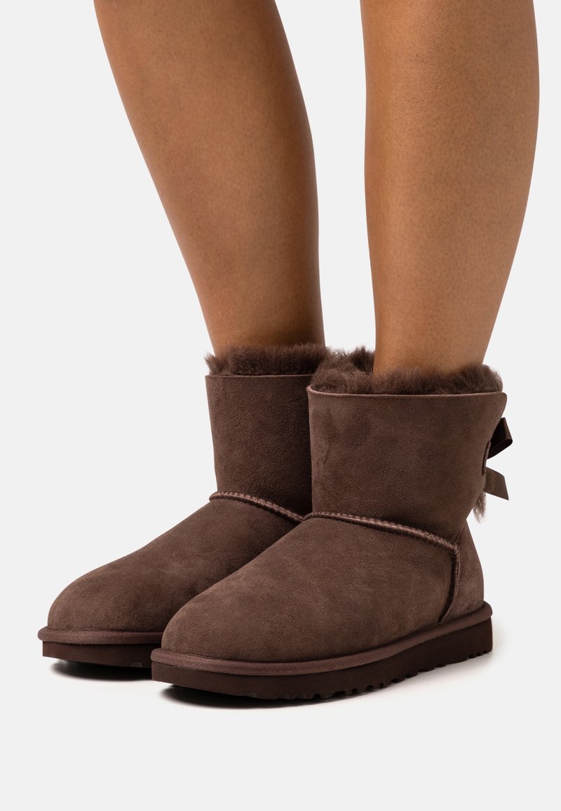 Bruna mocka ankelboots med en mjuk, fluffig foder och en liten rosett på baksidan, med en platt gummisula.
