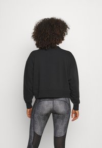 Sweat-shirt noir ample avec ourlet et poignets côtelés, associé à des leggings noirs imprimés arborant un motif répétitif du logo de la marque.