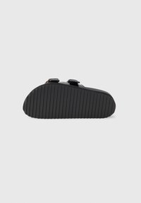 Crna sandala s dvije podesive remenčiće i teksturiranim crnim gumenim potplatom s vodoravnim utorima za prianjanje. Glatki materijal s minimalnim detaljima.