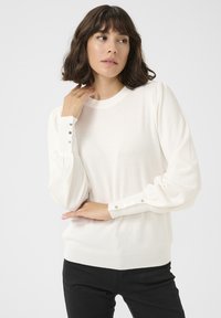 Pulover alb cu mâneci tip balon, cu manșete cu rigle și butoane argintii, având un decolteu simplu la gât. Material tricotat moale și ușor.