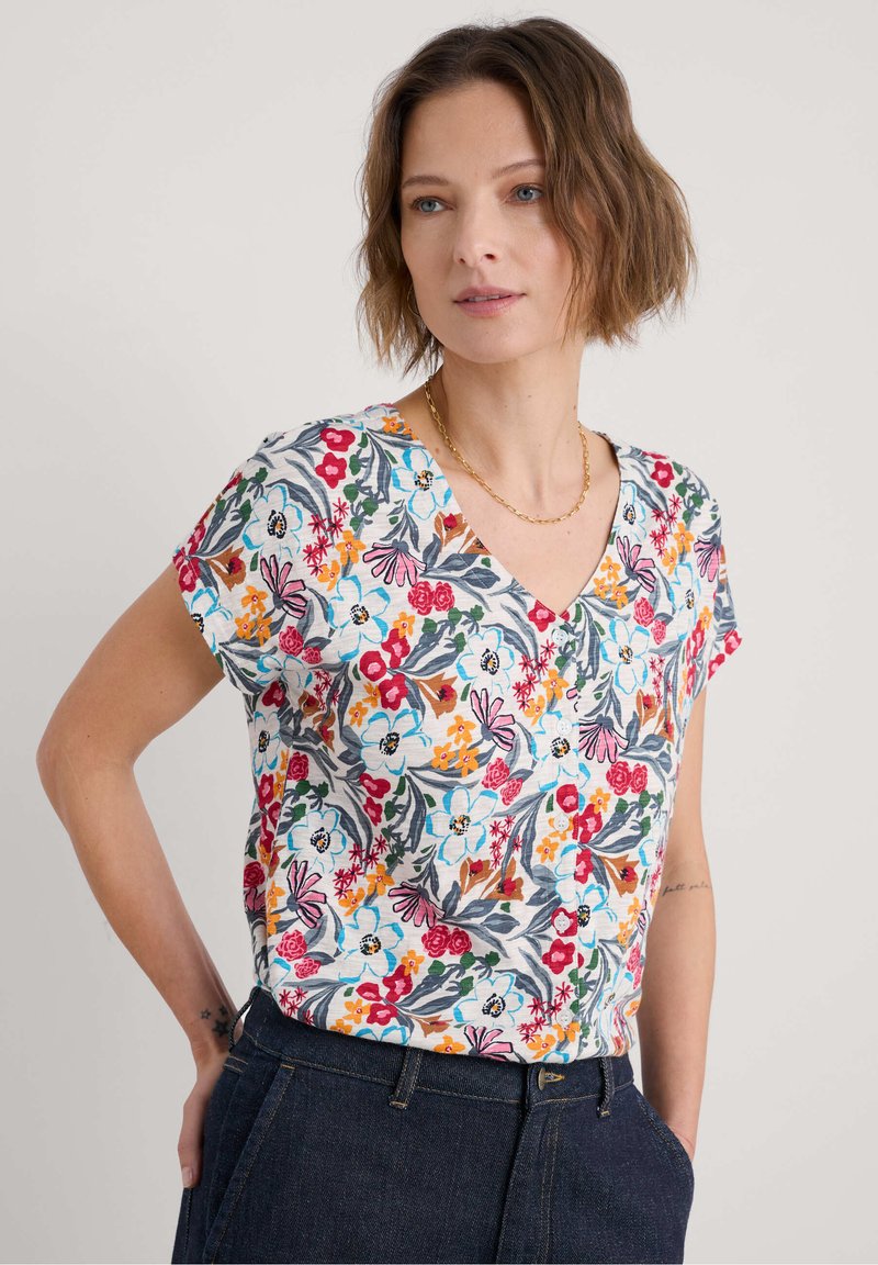 Gėlių trumpomis rankovėmis palaidinė su V formos iškirpte, iš šviesaus fono su daugiaspalviu raštu, pagaminta iš minkštos medvilnės.