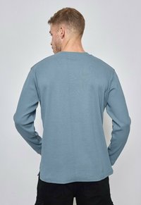 T-shirt à manches longues de couleur bleu doux, fabriqué en coton, avec un col rond et un design simple et droit.