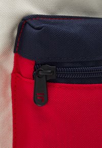 Angolo di una borsa in tessuto rosso e blu con una tasca con zip. Materiale in tela texturizzata con una zip nera visibile e cuciture dettagliate.