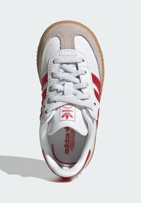 White leather sneaker with red accents and suede detailing. Features a textured gum sole and woven laces. Classic three-stripe design.