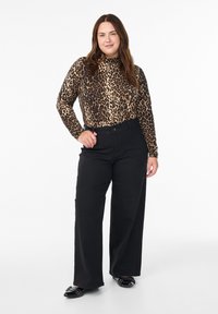 Majica dugih rukava s uzorkom leoparda, crne široke hlače, crne ravne cipele s detaljima. Glatka tkanina, prilagođena majica, klasičan kroj.