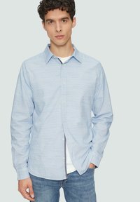 Jasnoniebieska koszula z długim rękawem, z kołnierzykiem zapinanym na guziki, o teksturowanej tkaninie i subtelny wzór w paski, noszona na białej koszulce.