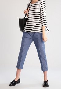 Pruhovaný černo-bílý top s třičtvrtinovými rukávy, doplněný světle modrými zkrácenými kalhotami a černými mokasíny. Černá kabelka na rameno zvýrazňuje celý outfit.