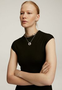 Top negro ajustado con mangas tipo manga corta, collares de cadenas de plata con colgantes en capas y pendientes de aro de plata colgantes. Textura de tela suave.