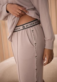 Šviesiai rožinė namų drabužių komplektas iš ribbingo audinio, su juodu elastiniu juosmens diržu su prekės ženklo logotipu ir šoninėmis kišenėmis.