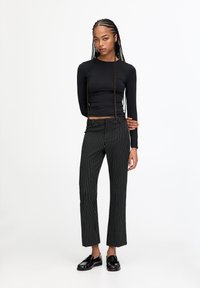 Top negru cu mâneci lungi asortat cu pantaloni evazați, în dungi verticale alb-negru, cu talie înaltă. Modelul poartă mocasini negri. Material neted.