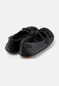 Bailarinas negras de cuero con una superficie texturizada, tiras elásticas y moños negros. Con puntera redondeada y suela de goma flexible.