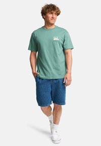 Groene katoenen t-shirt met een logo aan de voorkant, gecombineerd met denim shorts. Beschikt over een relaxte pasvorm en korte mouwen. Witte sneakers en sokken maken de look compleet.