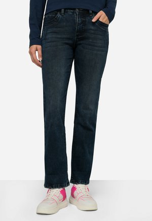Jeans bleu foncé en denim, avec une coupe droite, un léger délavage et des poches avant ; portés avec des baskets blanches et des accents roses.