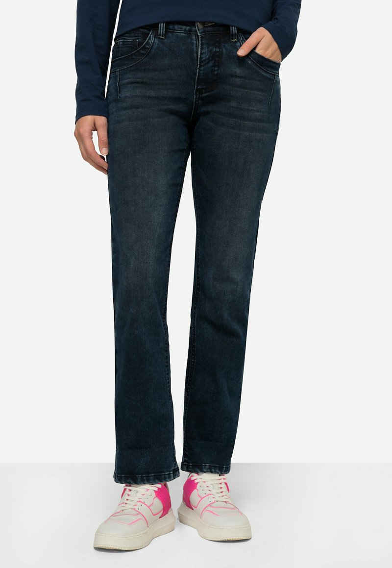 Jeans blu scuro in denim, con taglio dritto, leggera sfumatura e tasche frontali; indossati con sneaker bianche e dettagli rosa.
