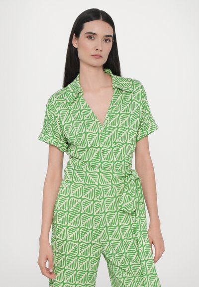 Combinaison verte à manches courtes, ornée d'un motif de feuilles dans une teinte plus claire. Elle a un col et un détail de taille nouée.