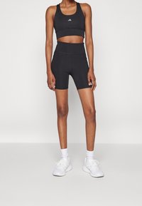 Top sportivo nero a metà vita e pantaloni corti a vita alta, realizzati in tessuto elasticizzato, abbinati a scarpe sportive bianche e calzini.