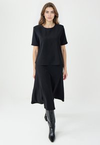 Czarny dwuczęściowy zestaw składający się z bluzki z krótkim rękawem i zwiewnej spódnicy, obie o gładkiej fakturze. Zestawiony z czarnymi kozakami do kolan.