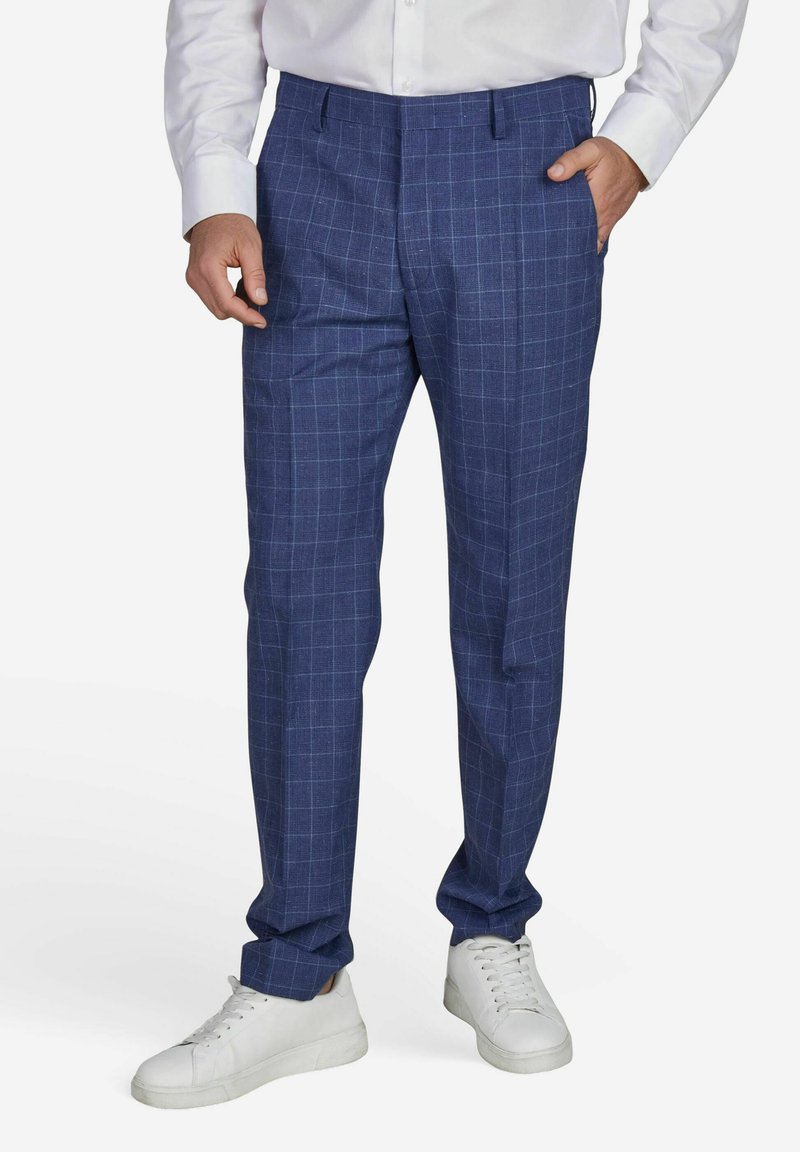 Navyblauwe op maat gemaakte broeken met een lichte ruitpatroon, voorzien van een plat voorkomen, zijzakken, en gedragen met witte sneakers.